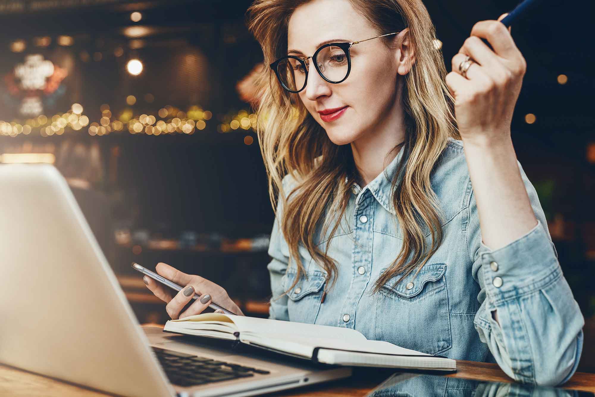 Student girl in trendy glasses sits in cafe in front of computer