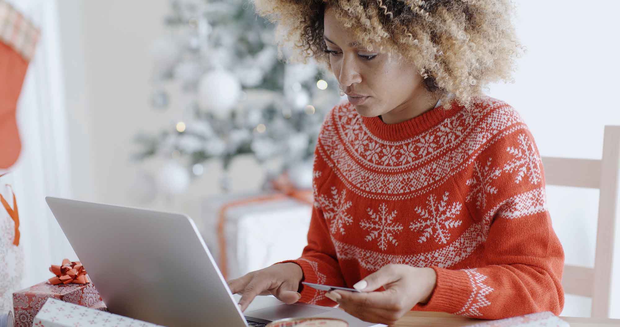 Women in holiday sweater in from of laptop with credit card.