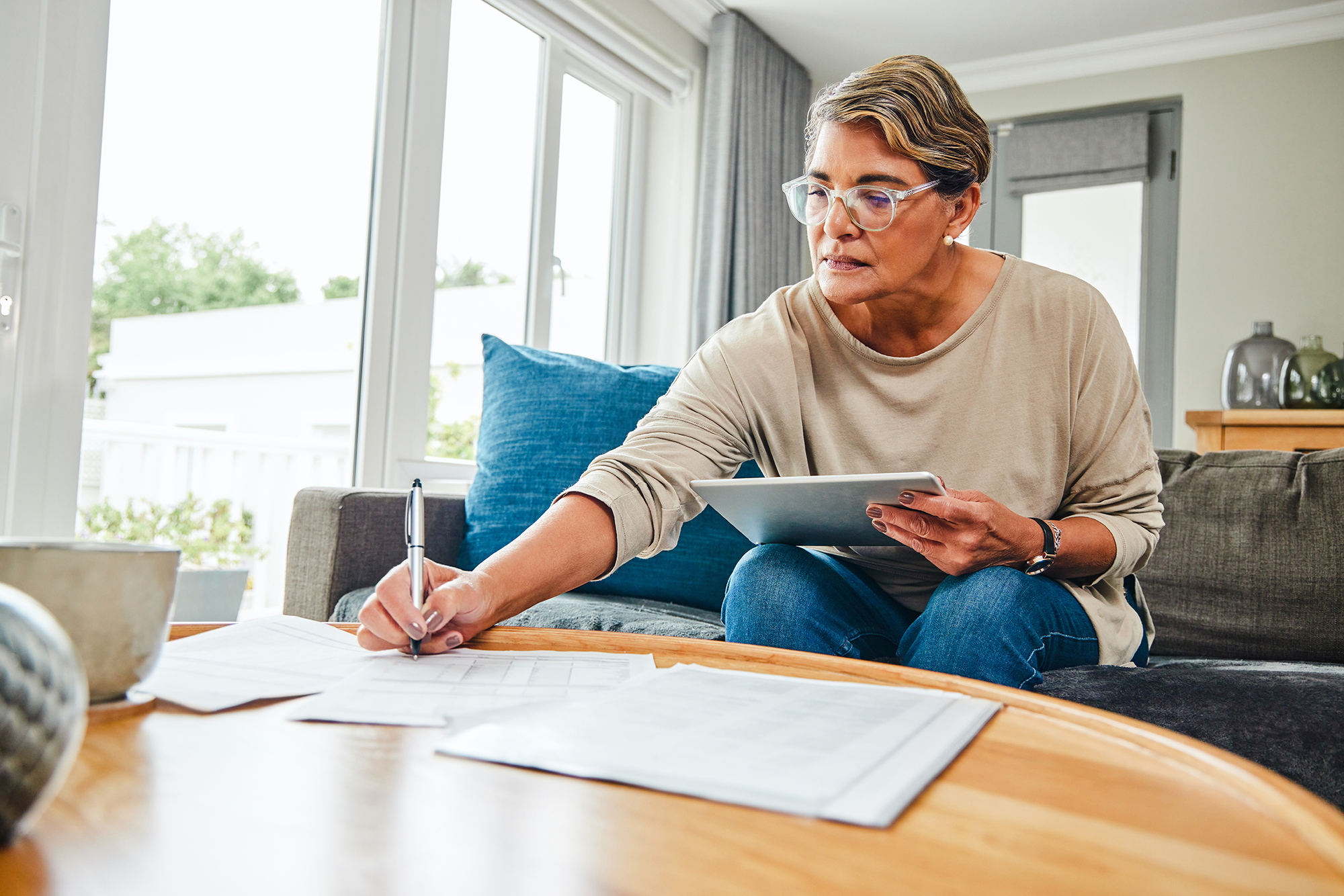 Shot of a mature woman using a digital tablet while going through paperwork at home