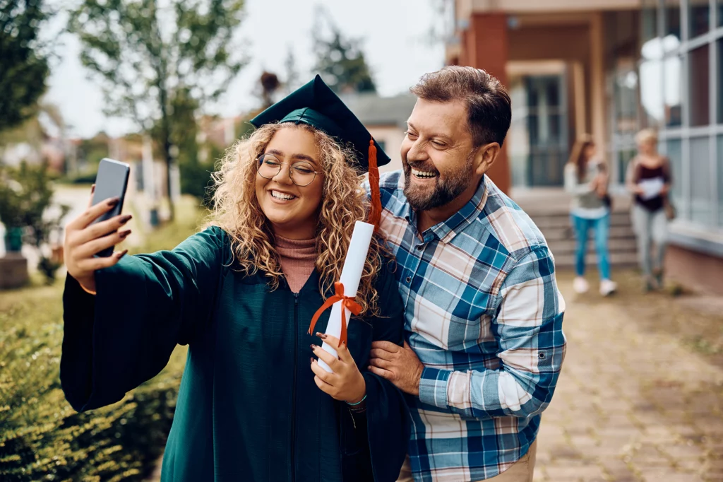 Happy university graduate and her father having fun while taking selfie with smart phone.