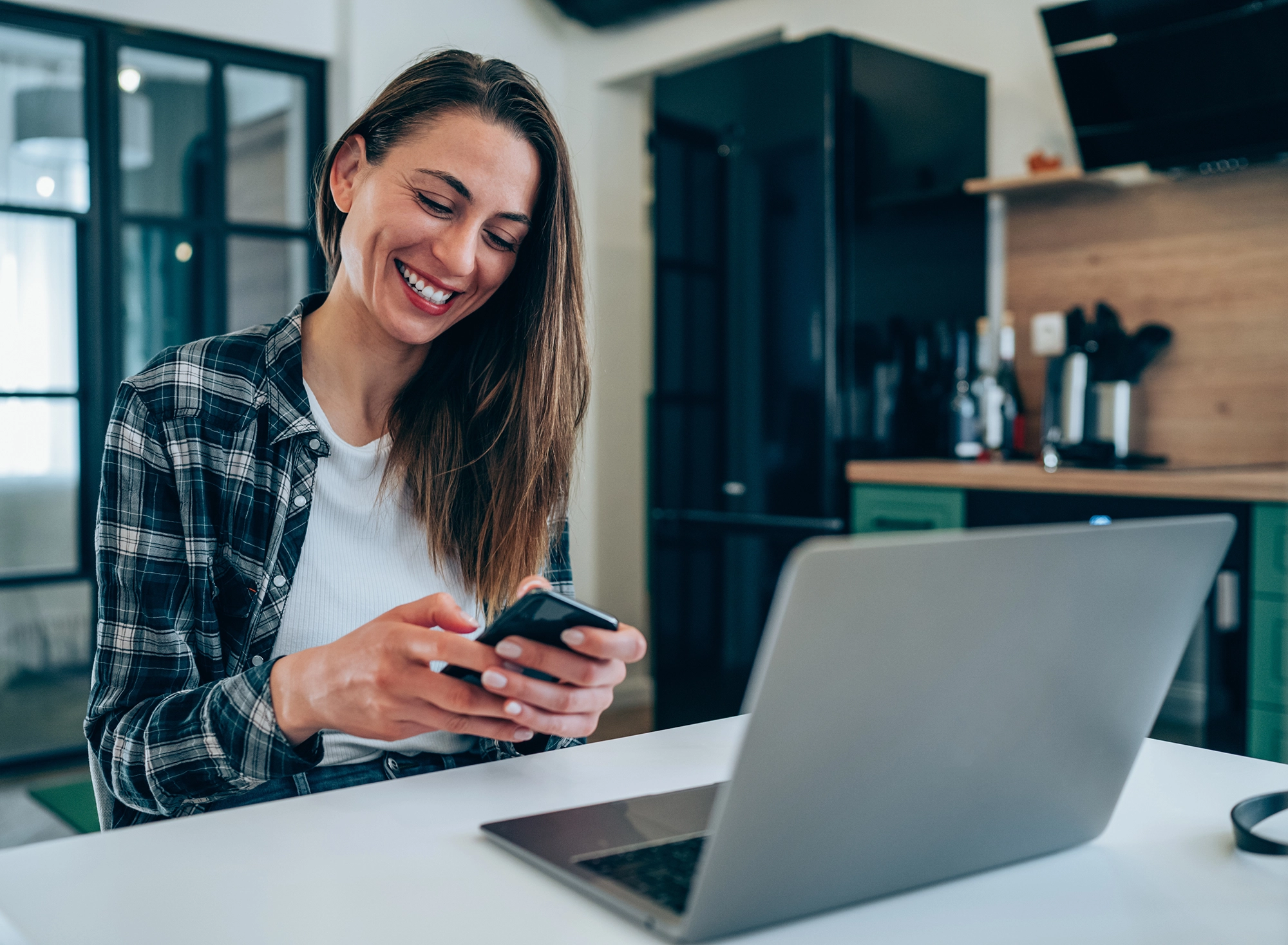 Woman looking at mobile phone in front of laptop