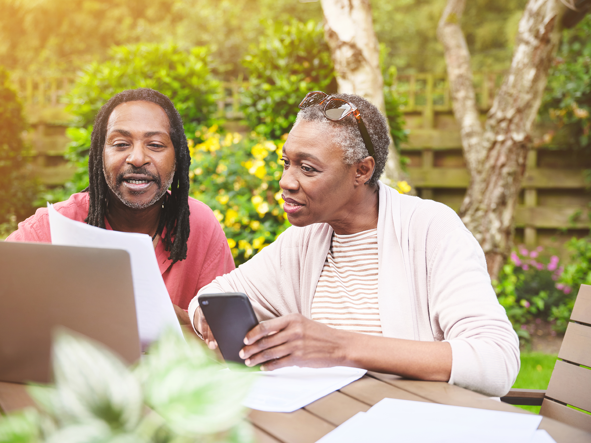 A senior couple using a laptop and going over paperwork in the garden at home.