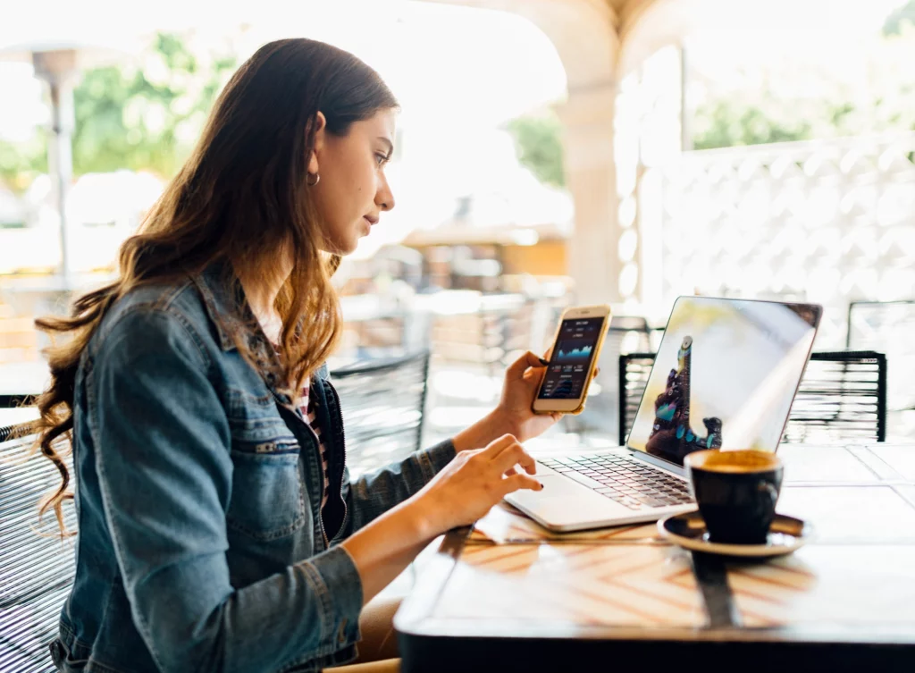 Young woman looking at her cell phone and laptop