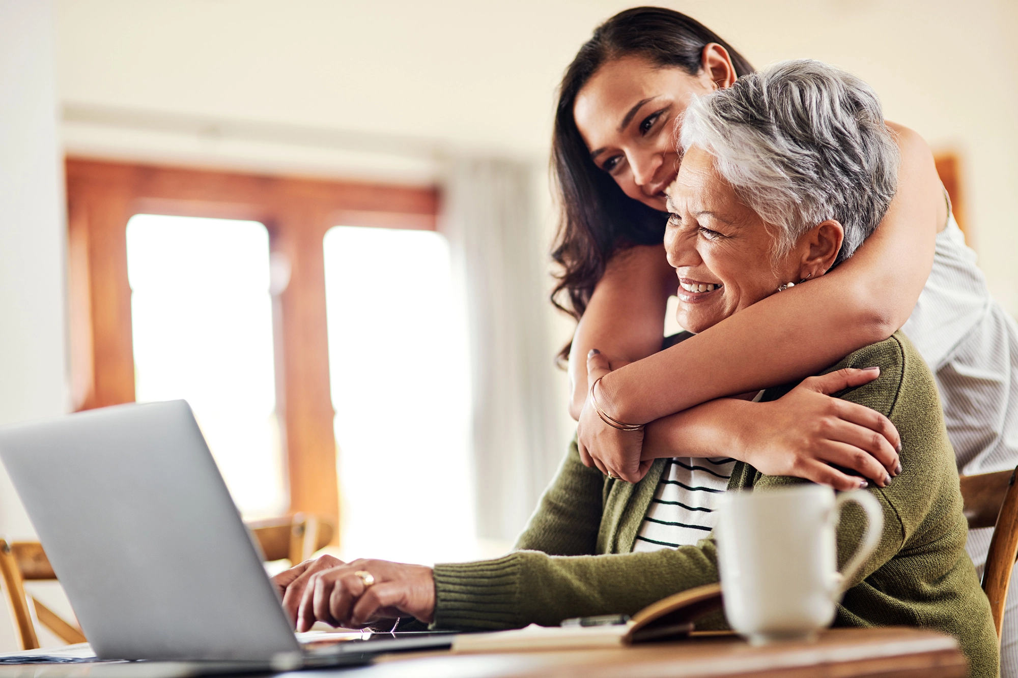 Daughter hugging mother in front of computer.