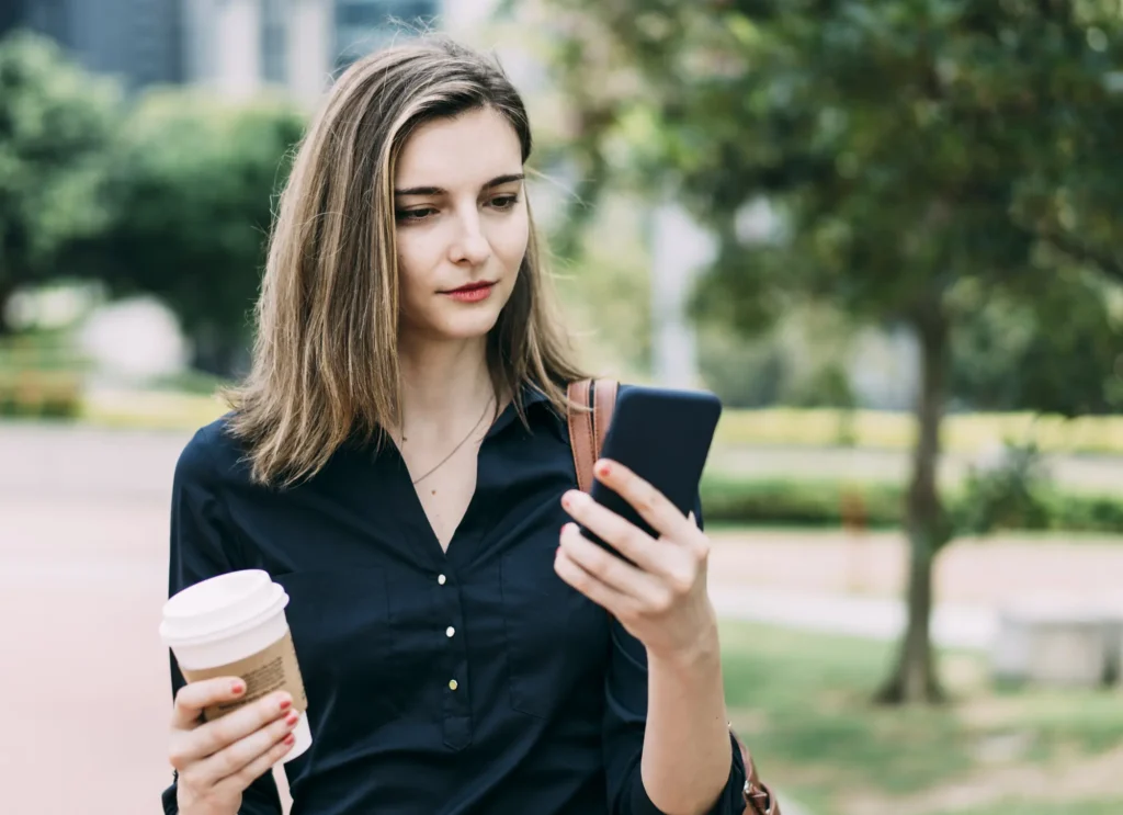 Young woman looking at her phone holder her coffee.