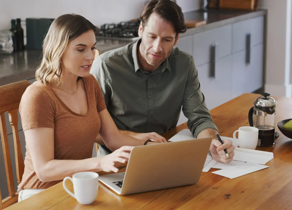 Couple sitting at kitchen table looking at laptop.