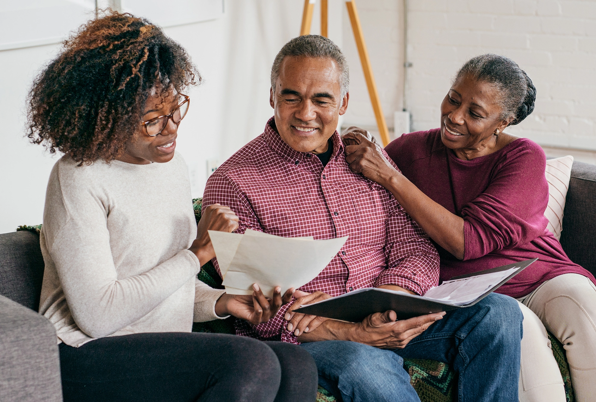 daughter, father and grandmother sitting on couch looking at paperwork and smiling