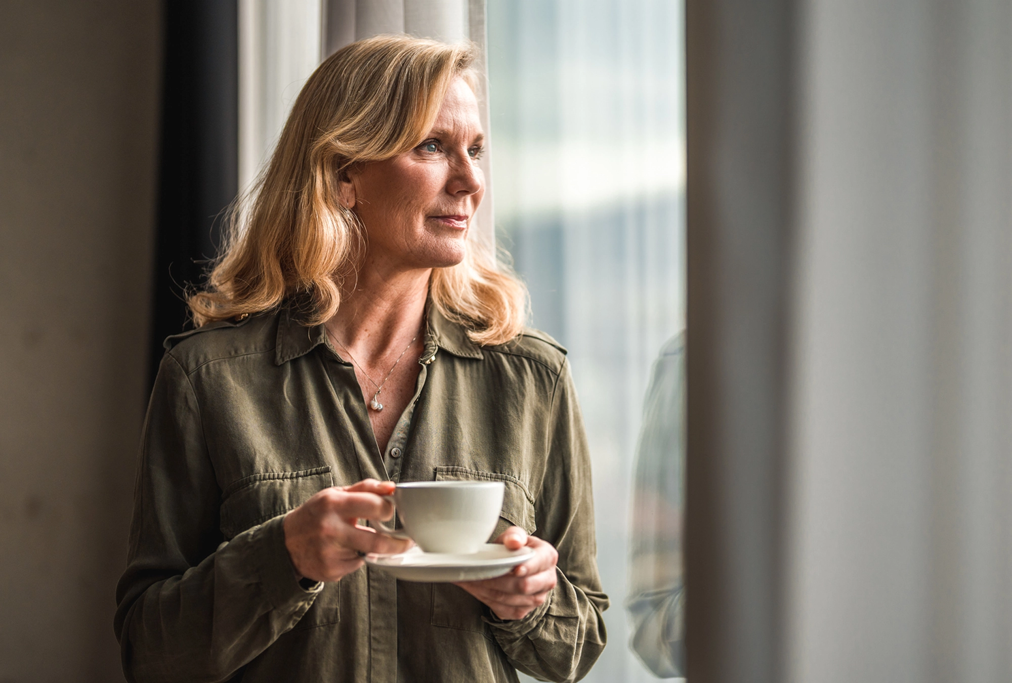 a woman is standing next to a window, drinking coffee